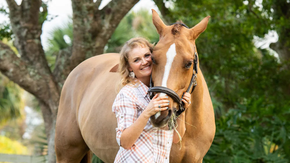 Jen standing next to a horse with a hay feeder in a grassy area.